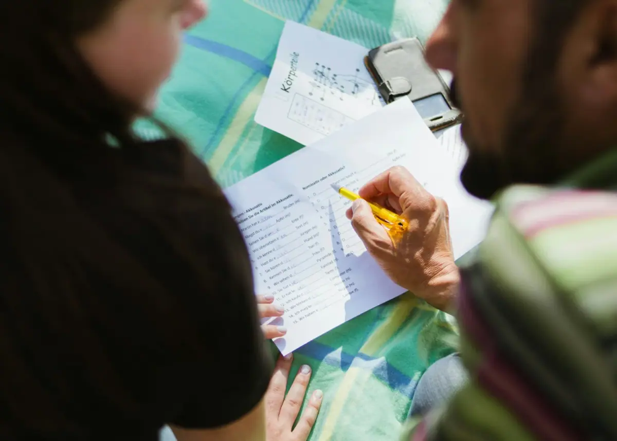 Two students working through a printed language exercise together, filling in answers by hand.