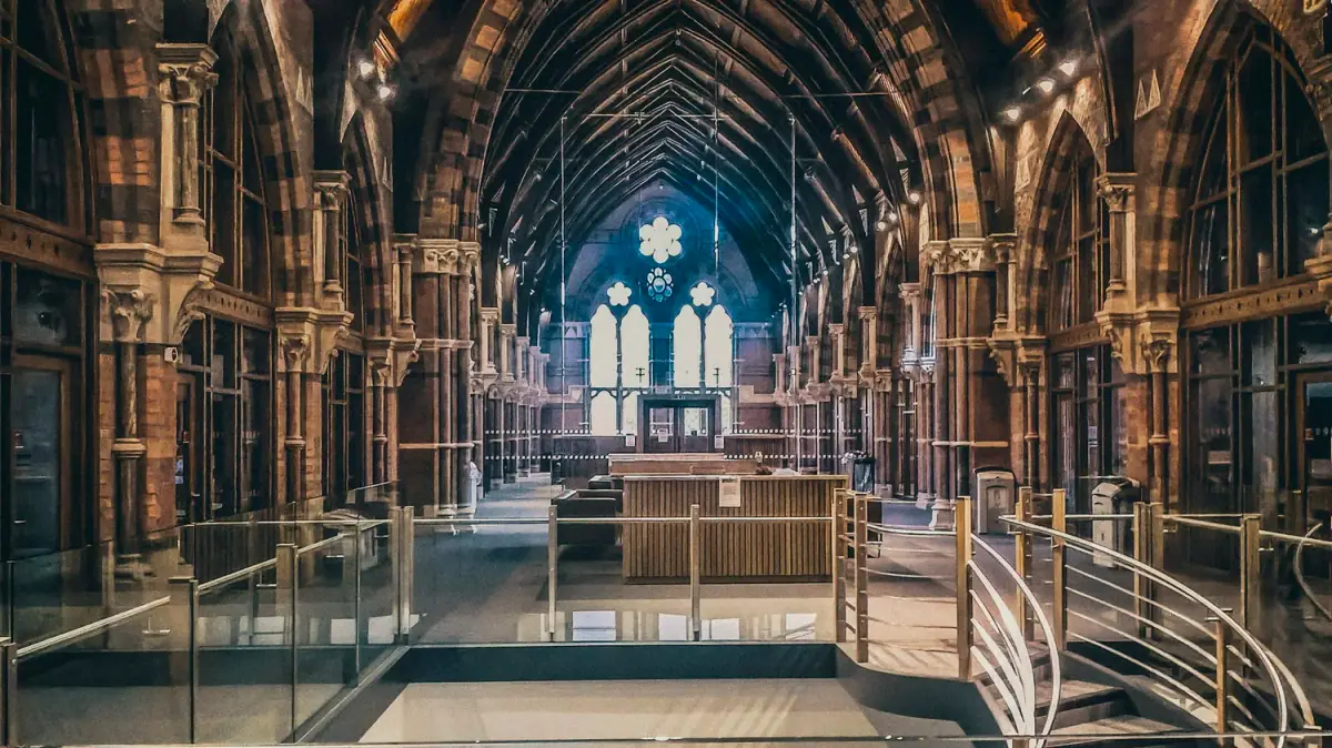 Interior of a historic church or cathedral with stained glass windows, high arched wooden ceilings, and intricate wood and stone architecture, with an area cordoned off by glass barriers.